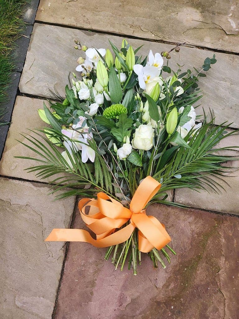 Presentation sheaf of white lilies, roses, orchids and palm foliage with a peach satin bow