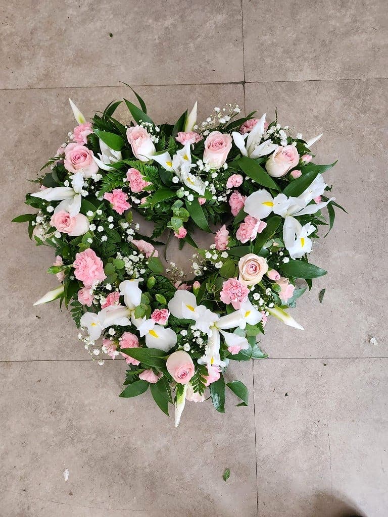 Heart-shaped wreath of pale pink roses, carnations, white irises and baby's breath on a tiled floor
