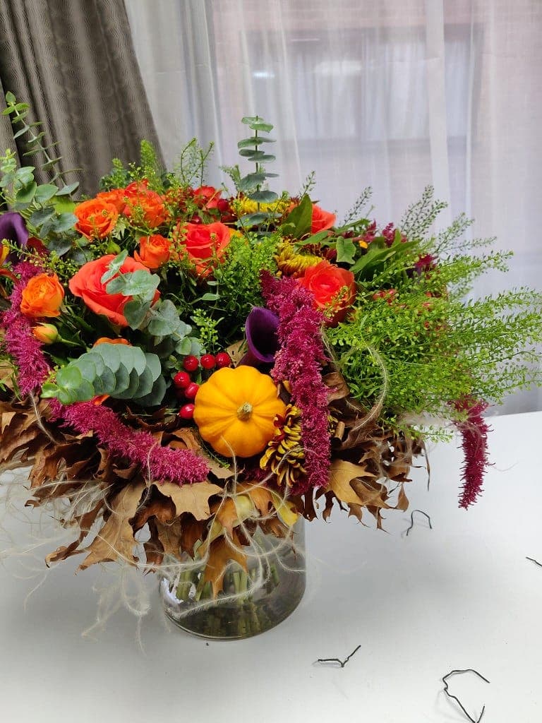 Autumnal arrangement of orange roses, purple calla lilies, hanging amaranthus and a mini pumpkin