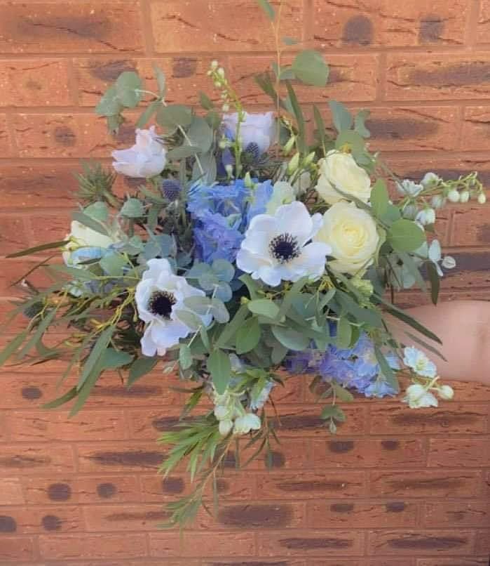 Hand-tied bouquet of white anemones, blue hydrangeas, cream roses and eryngium against a brick wall