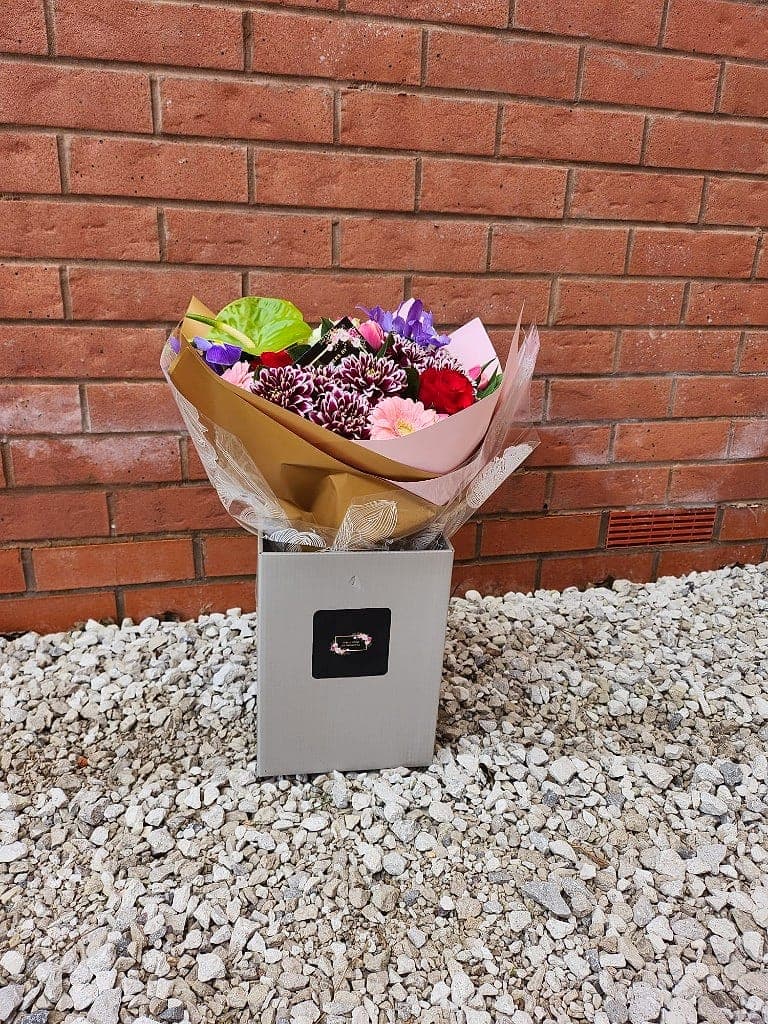 Gift box of burgundy chrysanthemums, a pink gerbera, purple irises and a lime anthurium leaf