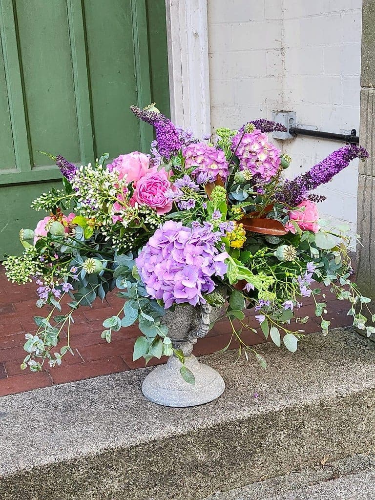 Garden-style urn of purple hydrangeas, pink roses and buddleia beside a garden door