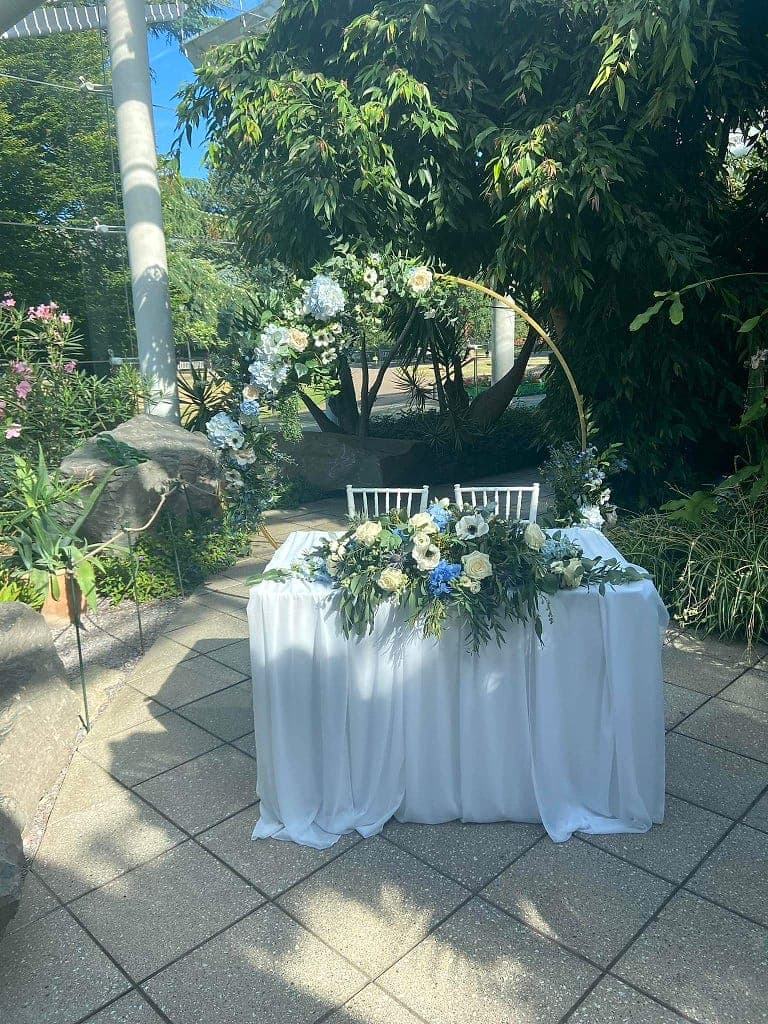 Outdoor wedding table with a white and blue floral runner and a gold hoop dressed on one side