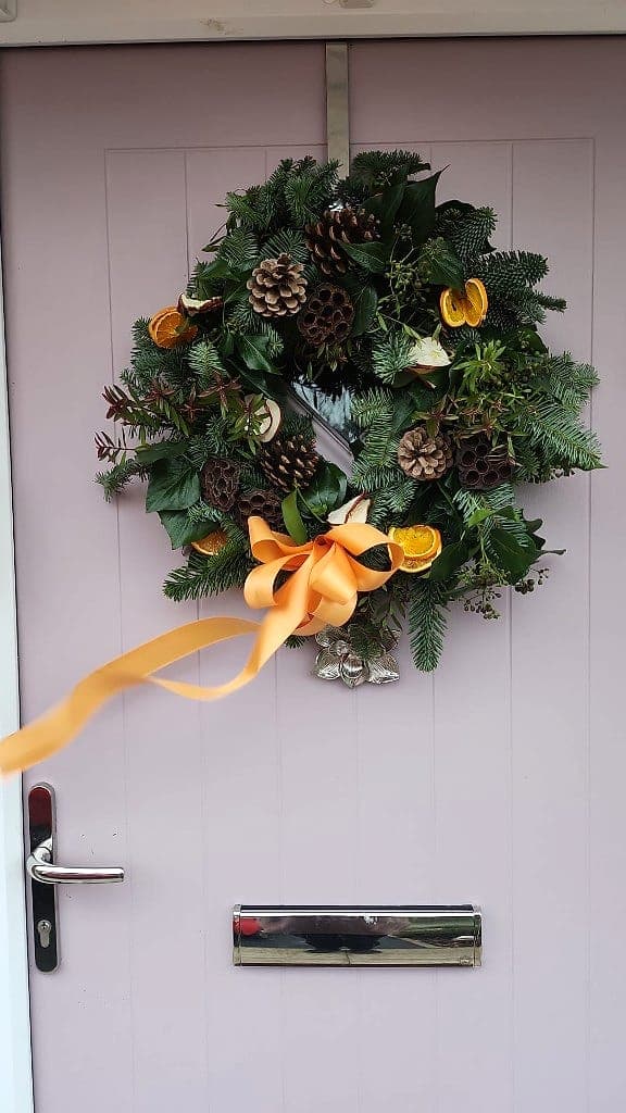 Evergreen door wreath with pinecones, dried orange slices and an apricot satin ribbon