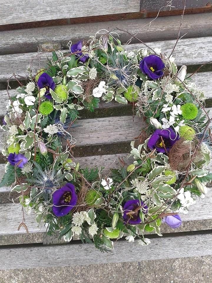 Circular wreath of purple lisianthus, lime chrysanthemums and sea holly on a wooden bench