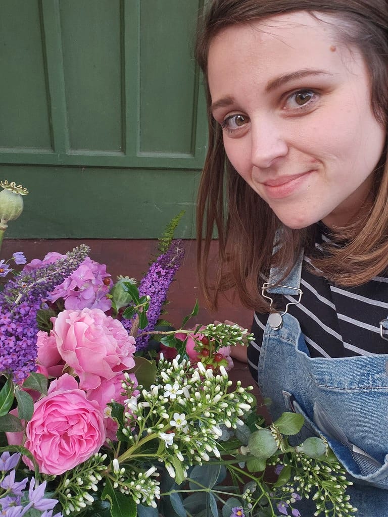 Megan, florist at Floral Vibe, with pink roses and purple buddleia, wearing dungarees