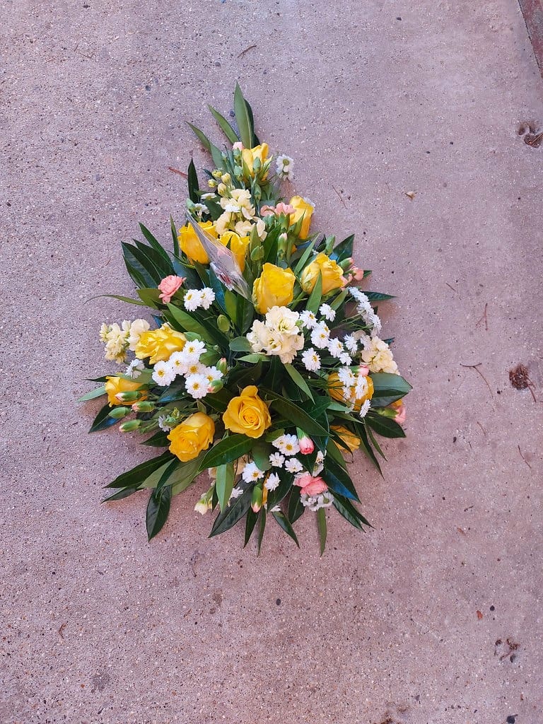 Classic teardrop funeral spray of yellow roses and cream stocks, laid with care